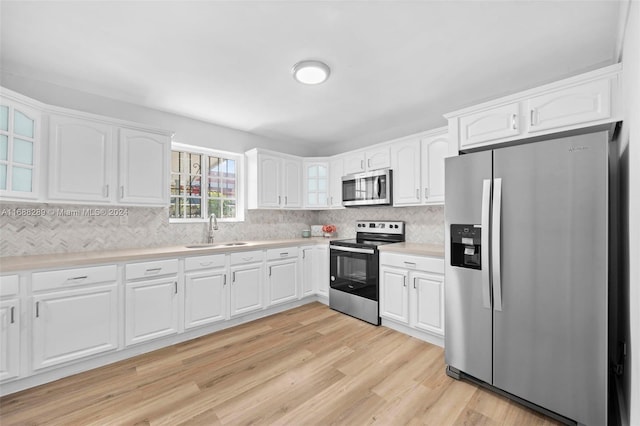 kitchen with sink, backsplash, light hardwood / wood-style floors, white cabinets, and appliances with stainless steel finishes