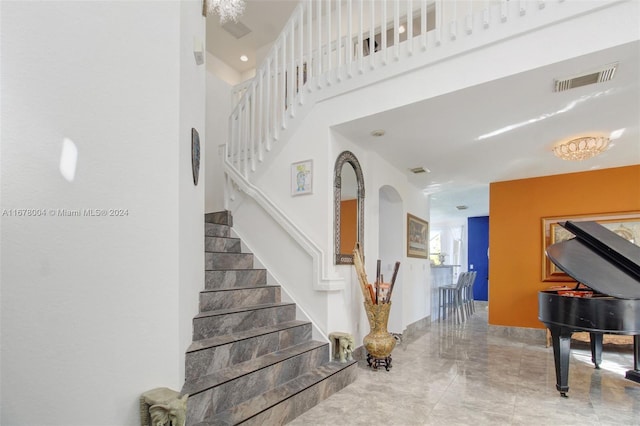 stairs featuring marble finish floor, a towering ceiling, and visible vents