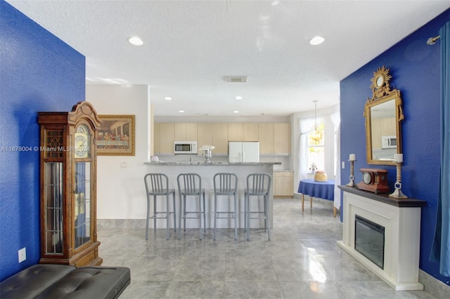 interior space featuring a peninsula, a breakfast bar area, light brown cabinetry, white appliances, and recessed lighting