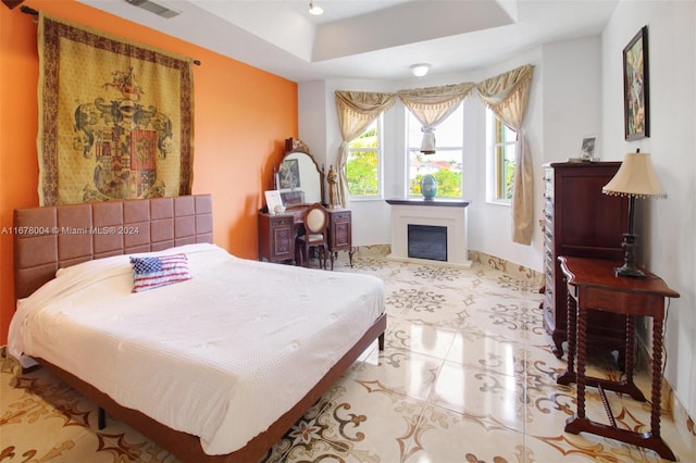 bedroom with baseboards, a fireplace, a tray ceiling, and visible vents