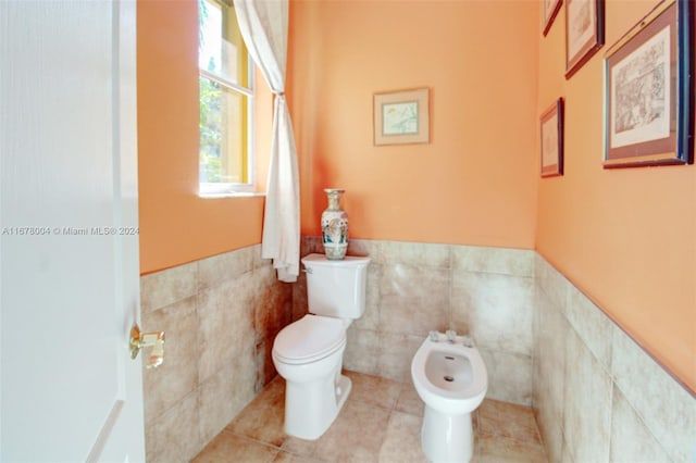 bathroom with tile walls, toilet, a wainscoted wall, a bidet, and tile patterned flooring
