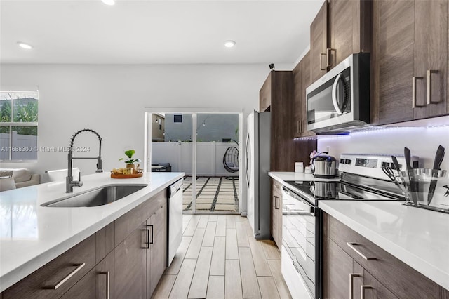 kitchen with dark brown cabinets, light hardwood / wood-style floors, stainless steel appliances, and sink