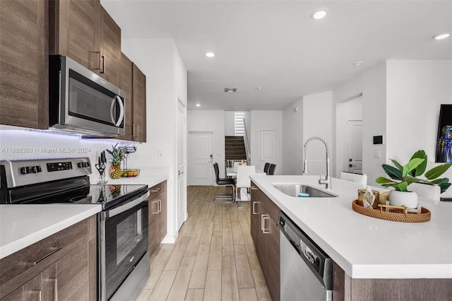 kitchen with a kitchen island with sink, appliances with stainless steel finishes, sink, and light hardwood / wood-style flooring