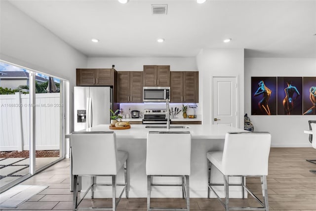 kitchen with a breakfast bar, light hardwood / wood-style floors, a center island with sink, and stainless steel appliances