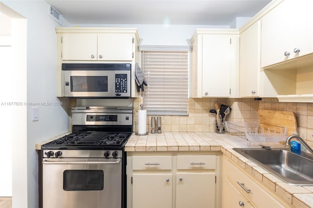 kitchen featuring tile countertops, tasteful backsplash, appliances with stainless steel finishes, and sink