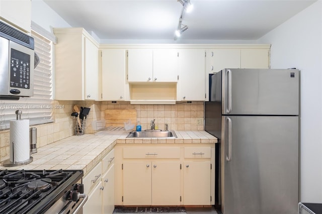 kitchen featuring tile countertops, decorative backsplash, sink, appliances with stainless steel finishes, and cream cabinetry