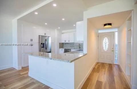 kitchen with light hardwood / wood-style floors, white cabinets, stainless steel refrigerator with ice dispenser, kitchen peninsula, and light stone countertops