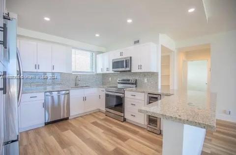 kitchen featuring white cabinetry, kitchen peninsula, appliances with stainless steel finishes, light stone countertops, and light hardwood / wood-style flooring