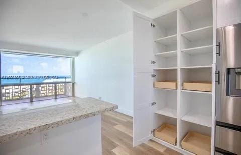 interior space featuring white cabinetry, light hardwood / wood-style floors, light stone counters, and stainless steel fridge with ice dispenser