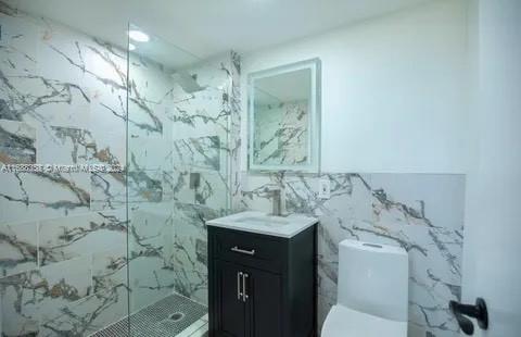 bathroom with tile walls, vanity, toilet, and a shower