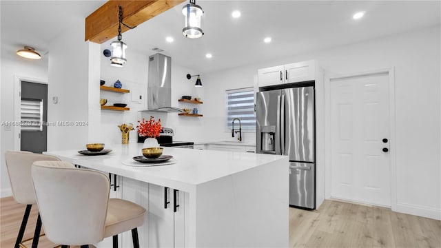 kitchen with white cabinets, light hardwood / wood-style floors, wall chimney range hood, and stainless steel fridge