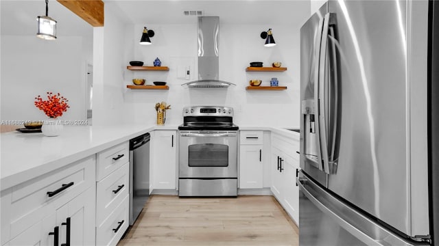 kitchen featuring light hardwood / wood-style floors, white cabinetry, appliances with stainless steel finishes, decorative light fixtures, and wall chimney range hood