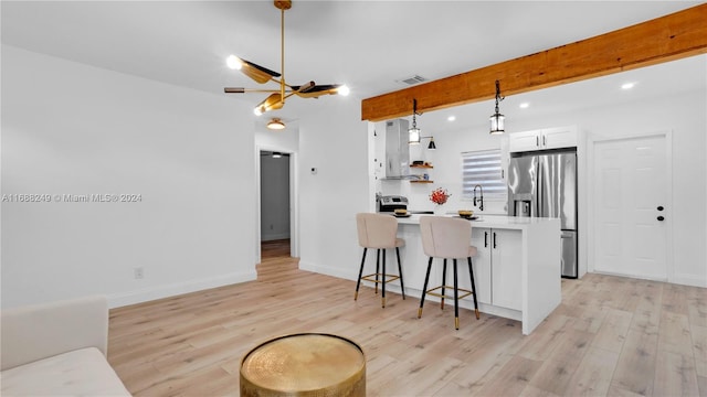 kitchen featuring appliances with stainless steel finishes, hanging light fixtures, a kitchen breakfast bar, white cabinets, and light hardwood / wood-style flooring