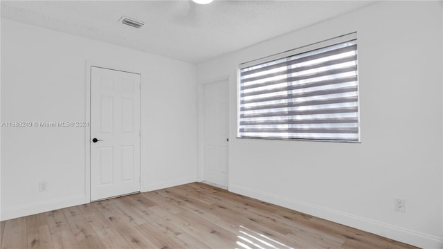 empty room with light wood-type flooring and a textured ceiling