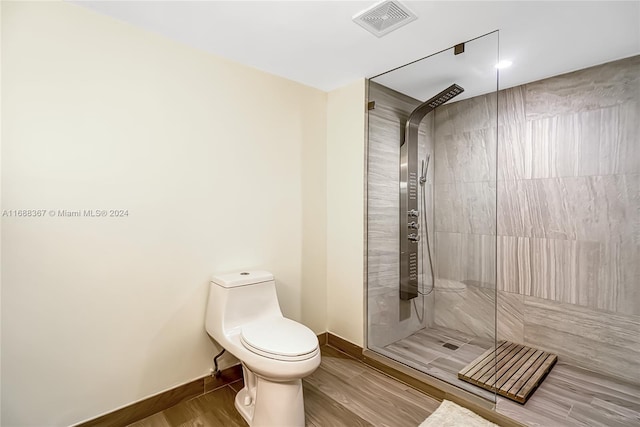 bathroom with hardwood / wood-style flooring, toilet, and a tile shower