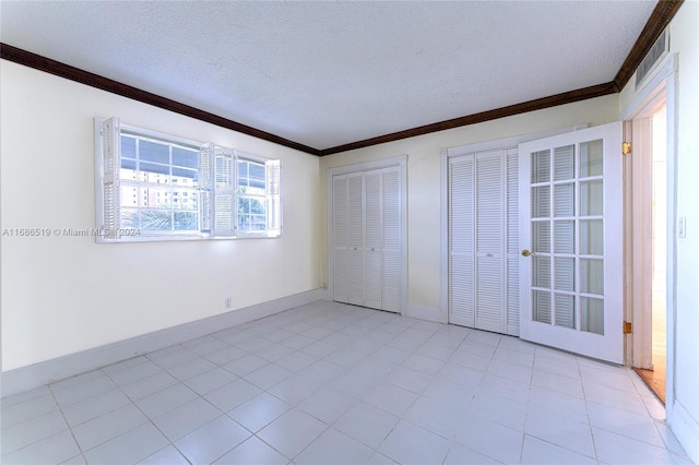 unfurnished bedroom with ornamental molding, a textured ceiling, light tile patterned floors, and multiple closets