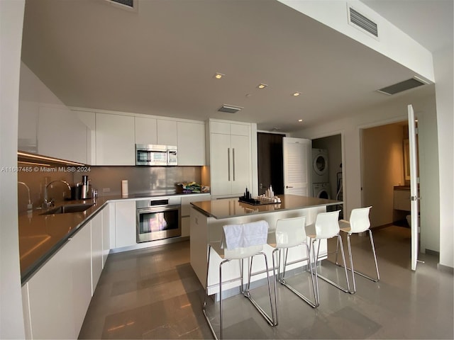 kitchen with stacked washer and clothes dryer, a kitchen island, appliances with stainless steel finishes, sink, and white cabinets