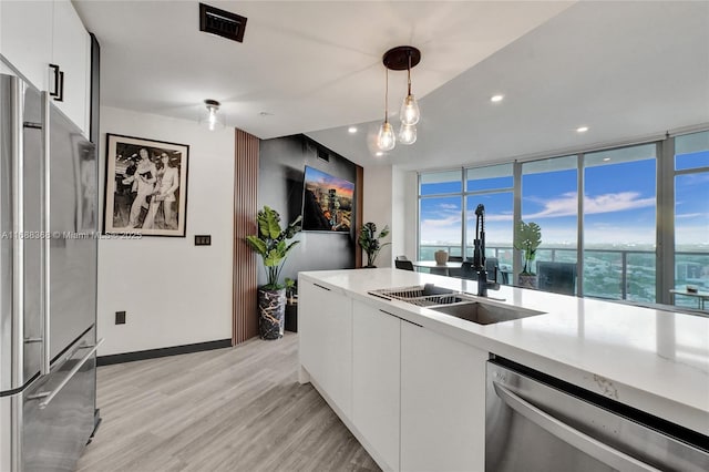 kitchen with light hardwood / wood-style floors, sink, hanging light fixtures, appliances with stainless steel finishes, and white cabinets