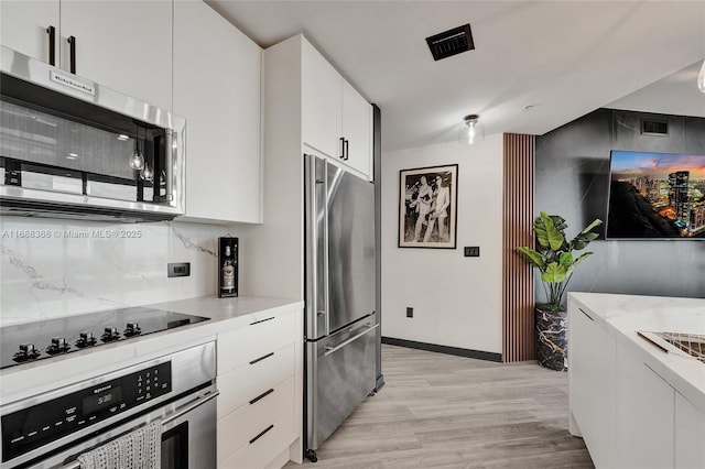 kitchen featuring light stone countertops, white cabinetry, stainless steel appliances, and light wood-type flooring