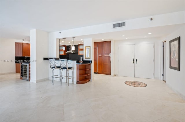 kitchen featuring beverage cooler, hanging light fixtures, a kitchen breakfast bar, wall chimney range hood, and backsplash