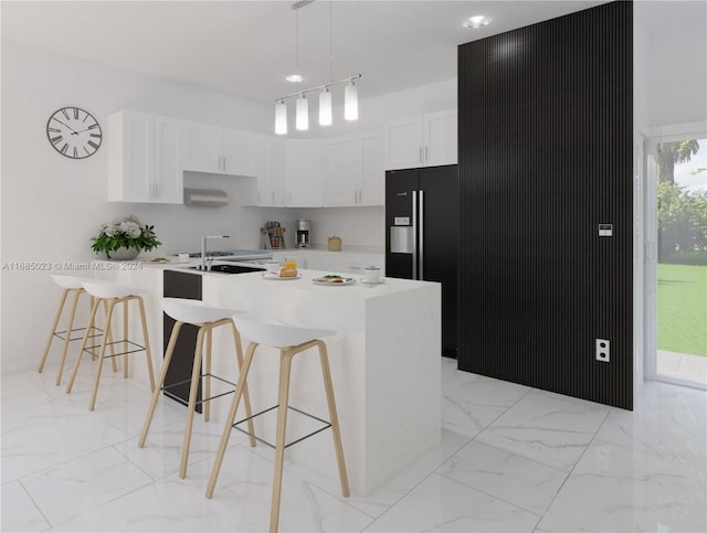 kitchen with black fridge, a center island with sink, white cabinets, hanging light fixtures, and a breakfast bar area