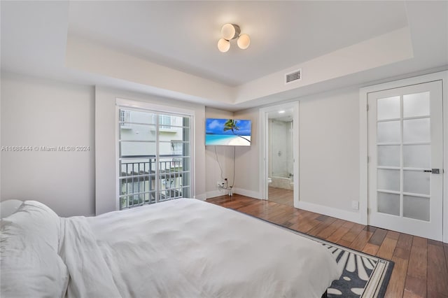 bedroom with a raised ceiling, connected bathroom, and wood-type flooring