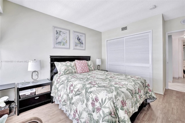 bedroom with a closet, light wood-type flooring, and a textured ceiling