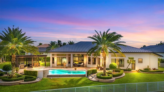 back house at dusk with a patio area, a swimming pool with hot tub, and a yard