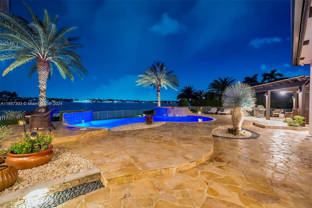 pool at twilight with a patio, a water view, and pool water feature