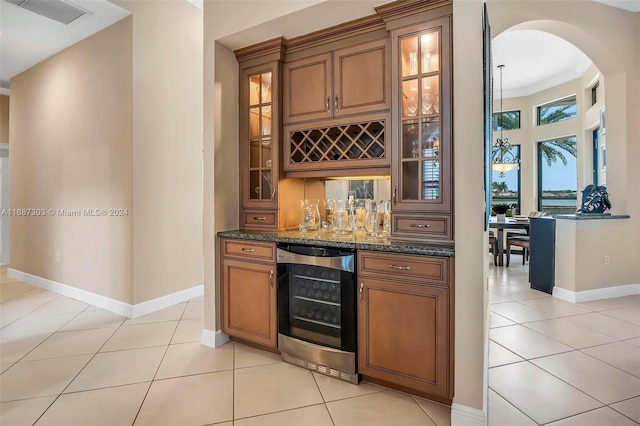 bar featuring dark stone countertops, light tile patterned floors, ornamental molding, and wine cooler