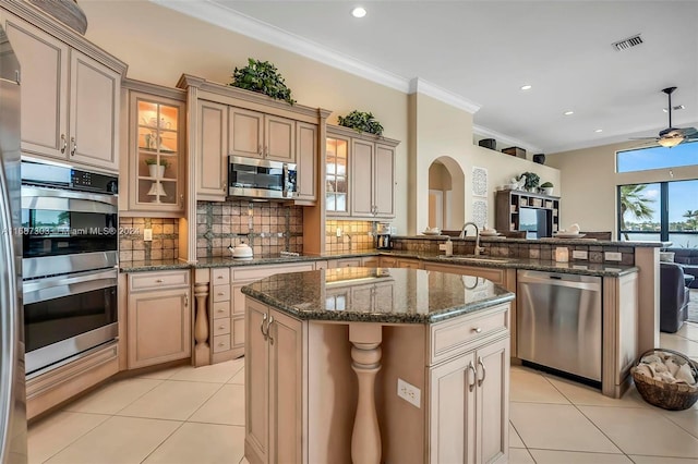 kitchen featuring a center island, sink, light tile patterned floors, ornamental molding, and appliances with stainless steel finishes