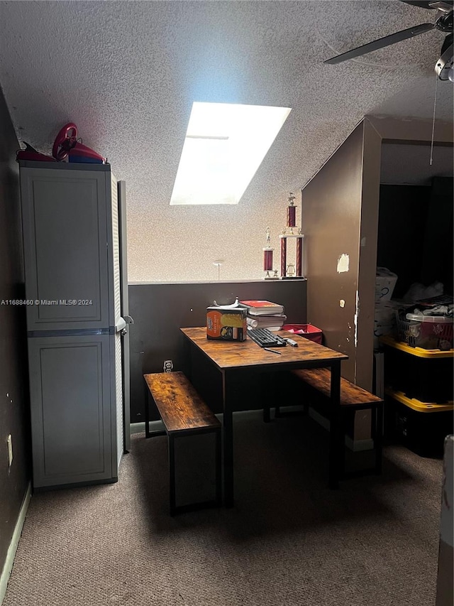 carpeted dining space featuring a textured ceiling, lofted ceiling with skylight, and ceiling fan