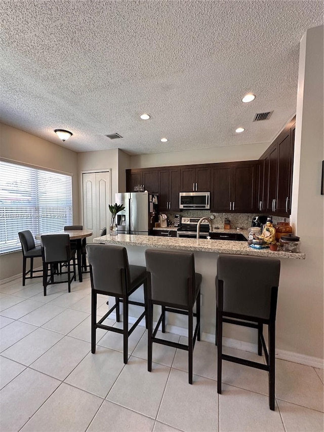 kitchen featuring kitchen peninsula, appliances with stainless steel finishes, a kitchen breakfast bar, a textured ceiling, and decorative backsplash