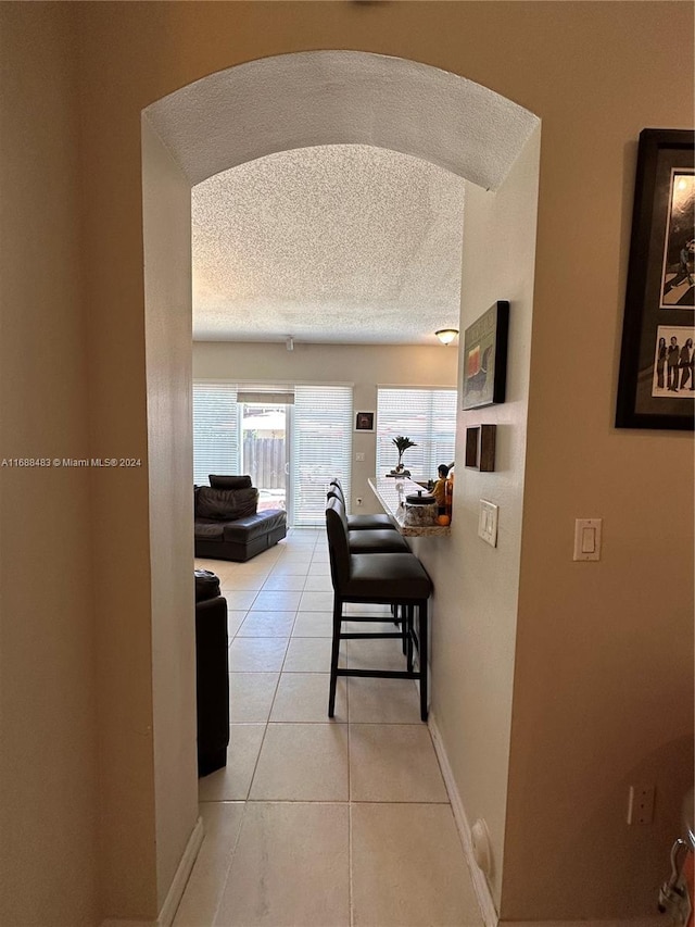 corridor featuring a textured ceiling and light tile patterned floors