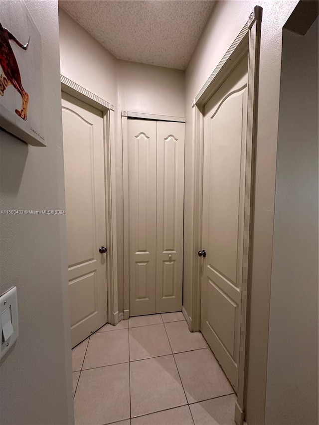 hall with a textured ceiling and light tile patterned floors