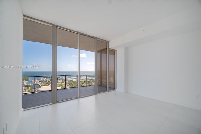 unfurnished room with a water view, a healthy amount of sunlight, floor to ceiling windows, and light tile patterned flooring