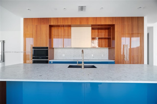 kitchen featuring sink, tasteful backsplash, double oven, and light stone countertops