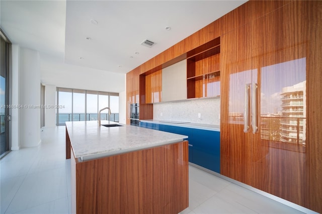 kitchen featuring black electric cooktop, sink, tasteful backsplash, light tile patterned floors, and an island with sink