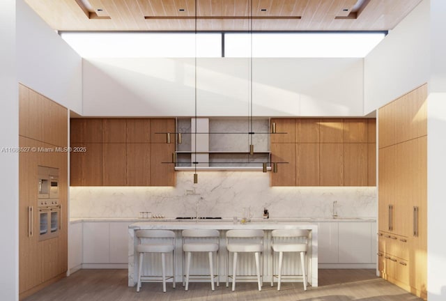 kitchen featuring sink, backsplash, oven, a kitchen bar, and light wood-type flooring