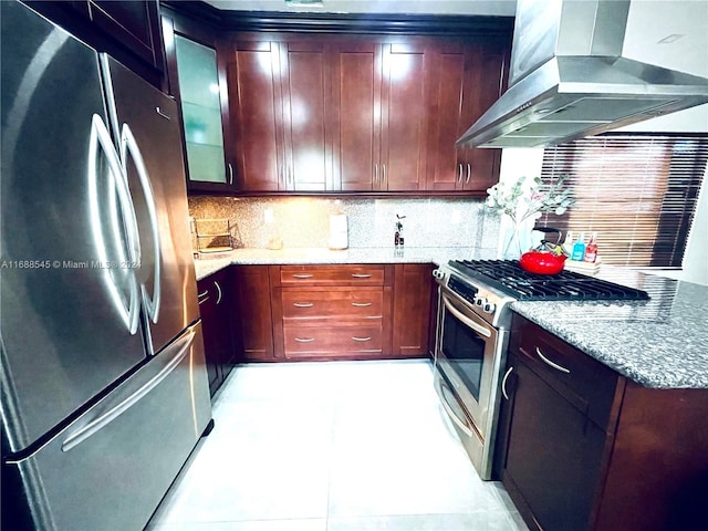 kitchen featuring stainless steel appliances, light stone counters, wall chimney exhaust hood, light tile patterned floors, and tasteful backsplash