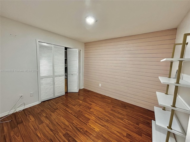 unfurnished bedroom featuring dark wood-type flooring, wooden walls, and a closet