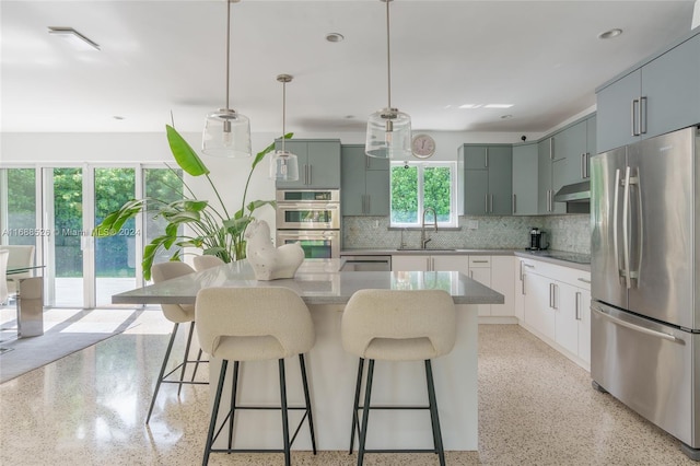 kitchen with a center island, sink, backsplash, appliances with stainless steel finishes, and decorative light fixtures