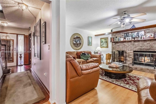 living room with a textured ceiling, a brick fireplace, hardwood / wood-style flooring, and ceiling fan