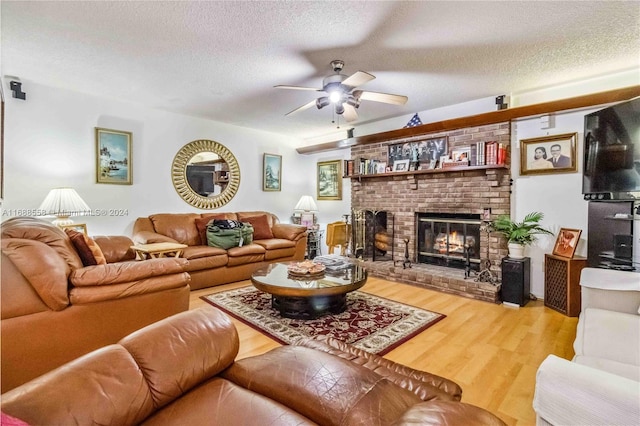 living room featuring hardwood / wood-style floors, ceiling fan, a textured ceiling, and a brick fireplace