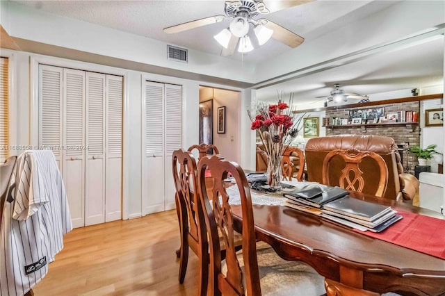 dining space with ceiling fan, a textured ceiling, light hardwood / wood-style floors, and a fireplace