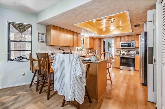 kitchen with appliances with stainless steel finishes, a kitchen bar, light hardwood / wood-style floors, and a raised ceiling