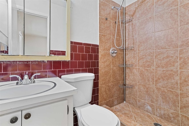 bathroom with vanity, tiled shower, tile walls, and toilet