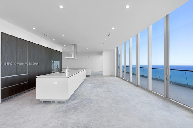 kitchen with a wall of windows, a center island with sink, sink, and a water view