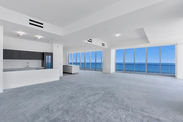 unfurnished living room with a tray ceiling, a water view, sink, and plenty of natural light