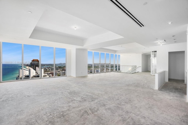 unfurnished living room featuring a tray ceiling, a water view, and floor to ceiling windows